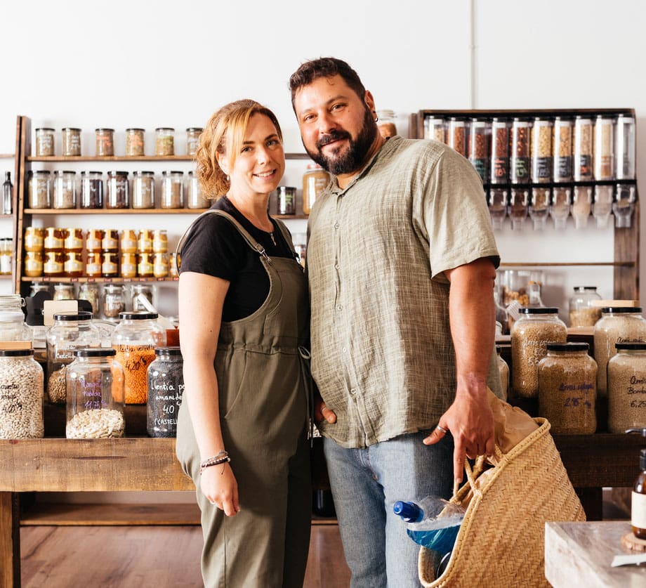 Smiling Couple Holding a Shopping Bag at a Bulk Grocery Store Full of Products