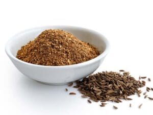 Ground cumin in white ceramic bowl isolated on white. Whole cumin.