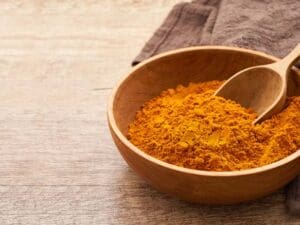 close up a pile of ground turmeric powder or curcumin powder in wood plate and scoop on wooden table background. turmeric or curcumin powder
